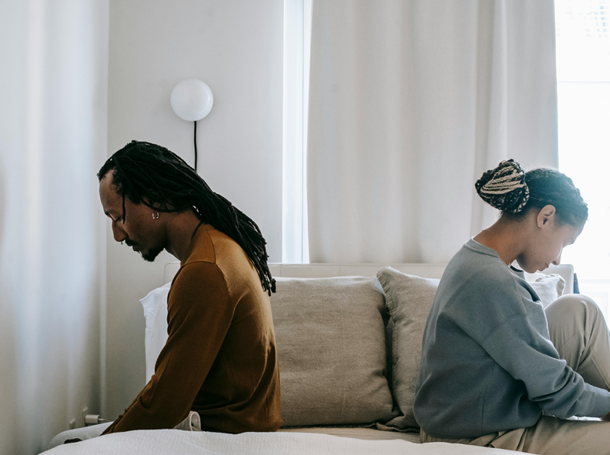 A couple sitting back to back on a bed, appearing emotionally distant, suggesting conflict or a breakup.